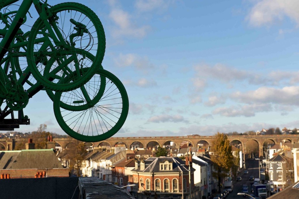 Green bike wheels against a blue sky, tower over the Brighton skyline