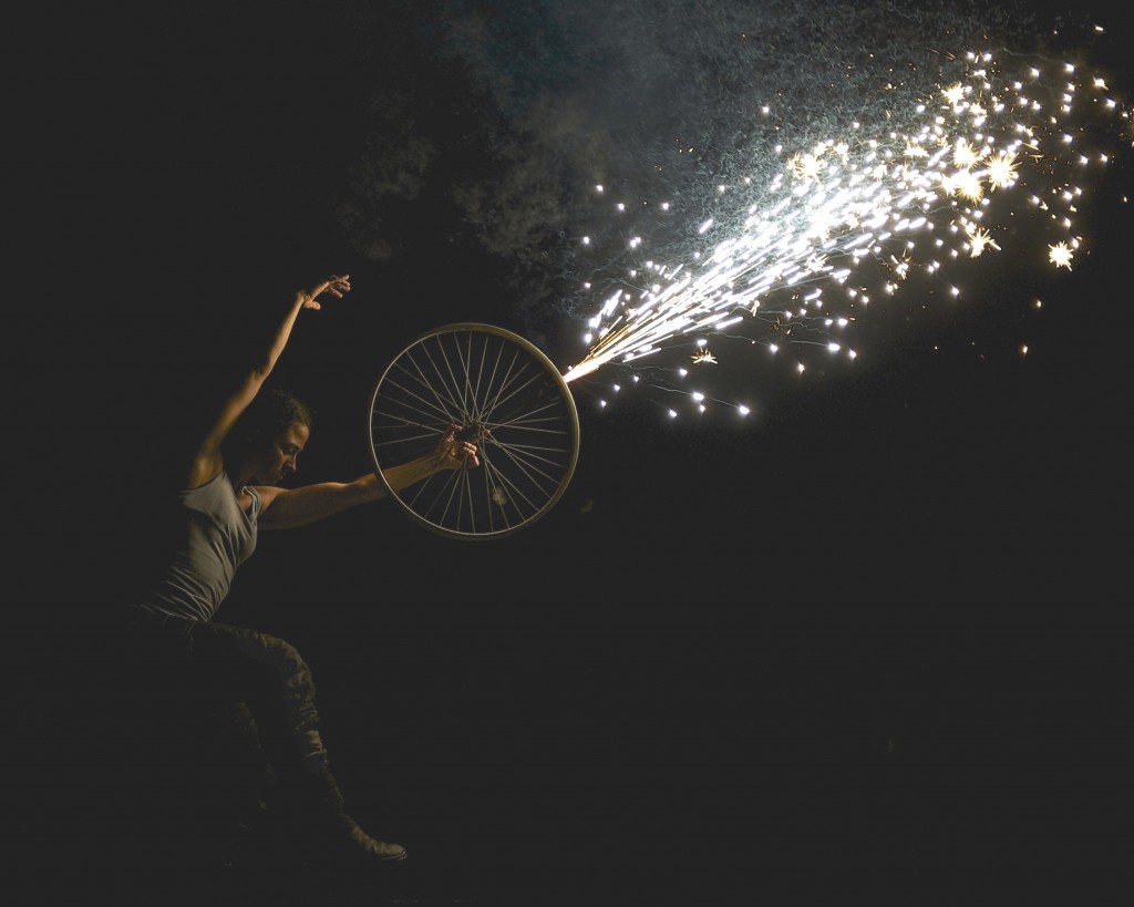 woman dances with a bike wheel from which shoots a sparkling firework (don't try this at home!)