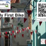 Small green child's bike at the top of a wall, with title, logos & QR code
